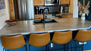 A modern kitchen with wooden cabinets, stainless steel appliances, and a bar area with stools.