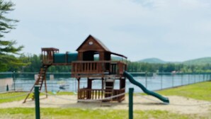 Une structure de jeux en bois, dotée d’un toboggan et d’une zone d’escalade, située près d’une étendue d’eau.