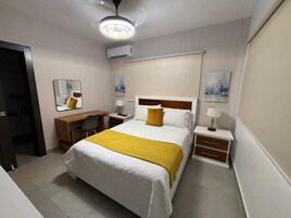 Quarto de hotel com cama, mesas de cabeceira, escrivaninha e uma cadeira.