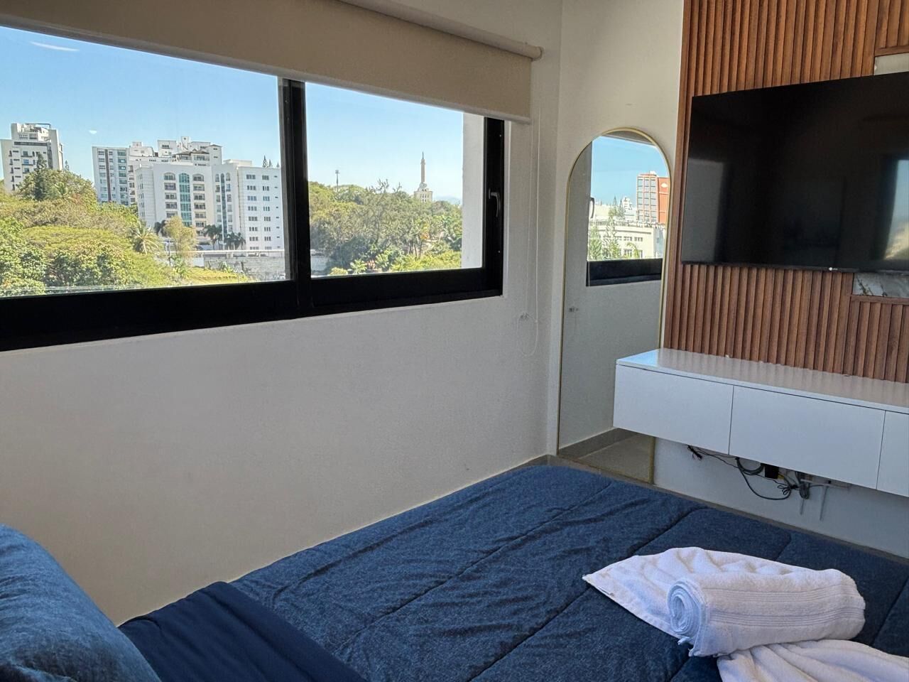 A hotel room with a bed, a TV, and a window with a city view.