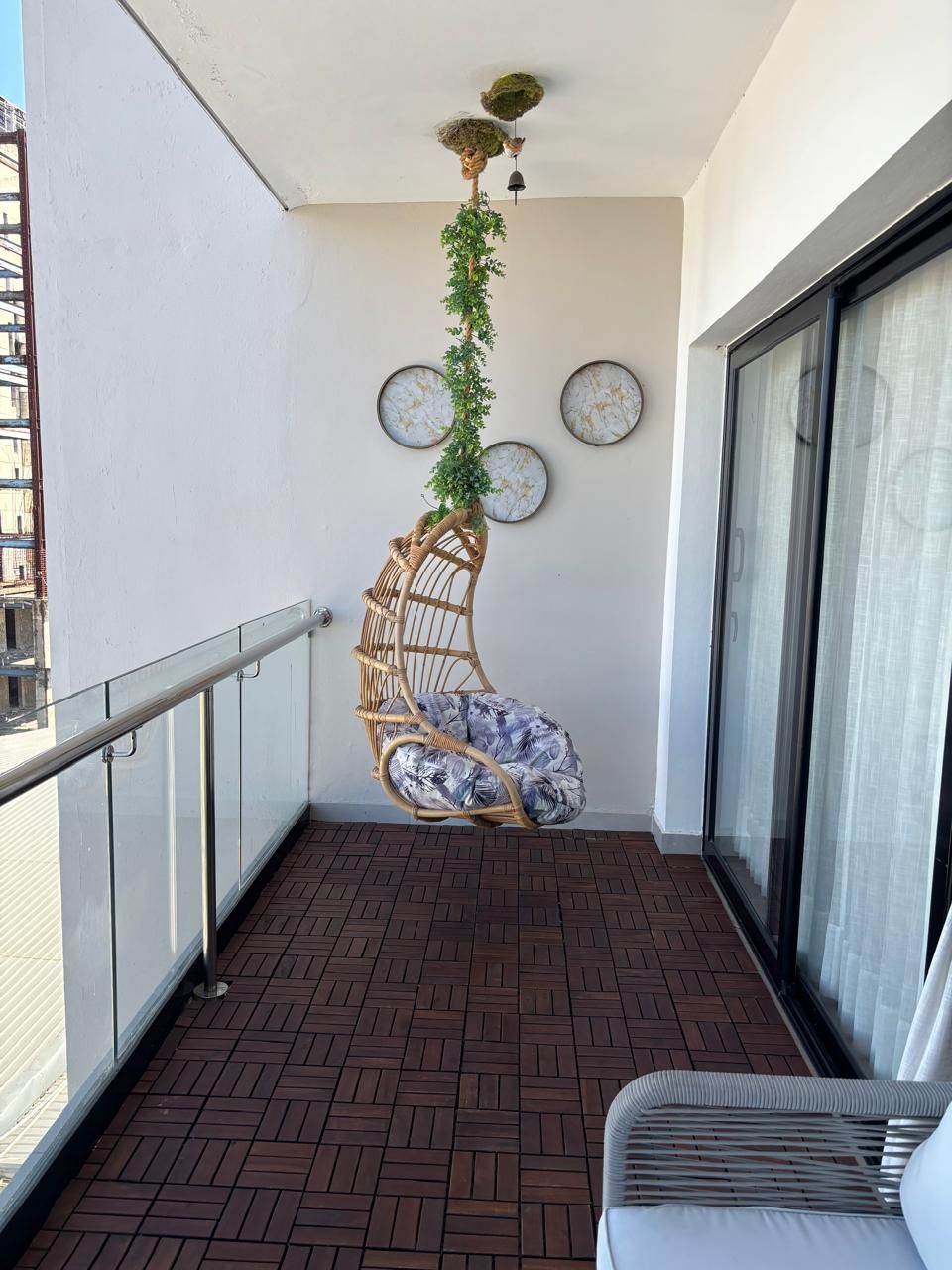 A balcony with a wicker chair, a hanging plant, and three wall-mounted round mirrors.