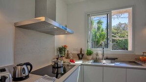 Una cocina moderna con armarios blancos, una tetera de acero inoxidable, un tostador y un ventanal con vistas a la vegetación.