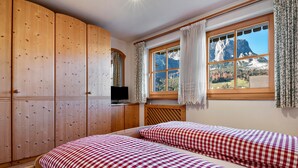 Una habitación con dos camas, un armario de madera, televisión y ventana con vista a la montaña.