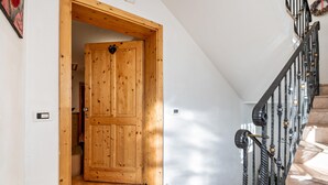 Una puerta de madera que da a una habitación, una escalera con barandilla metálica y un felpudo en la base.