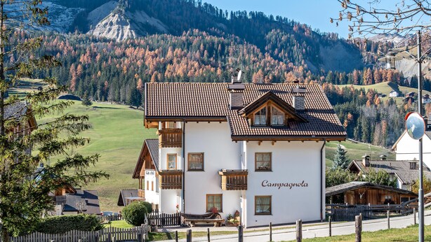Un edificio blanco con techo marrón, con la leyenda 'Camponola', rodeado de una cerca y con montañas al fondo.