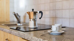 Una encimera de cocina con una cafetera, un lavabo y dos tazas blancas sobre platillos.