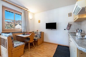 A compact kitchen with a wooden dining area, a TV mounted on the wall, and a view of the outdoors.
