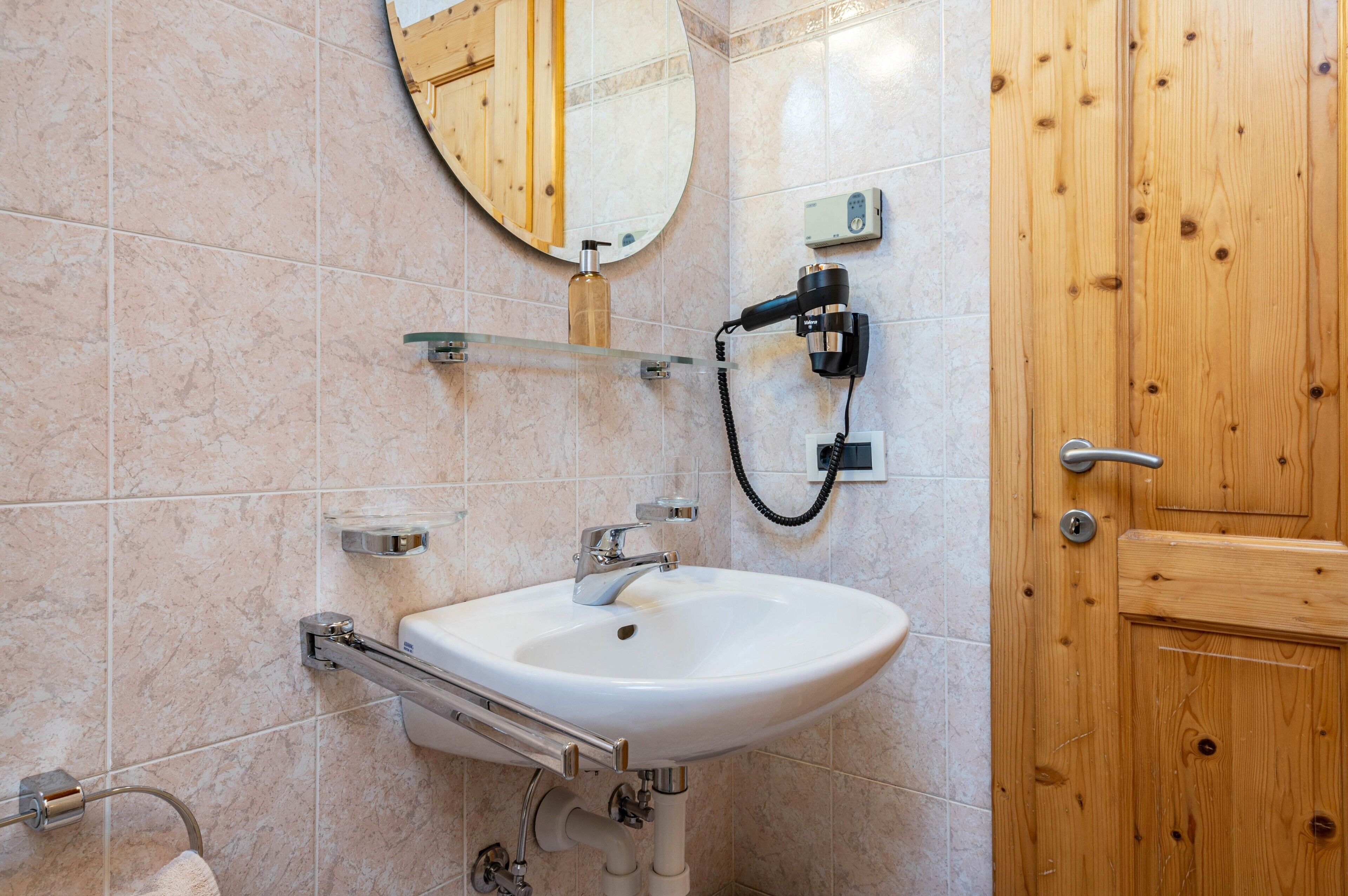 A bathroom with a white sink, a mirror, a wooden door, and a towel rack.