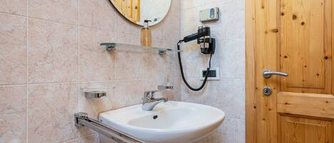 A bathroom with a white sink, a mirror, a wooden door, and a towel rack.