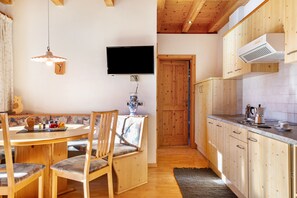 Una mesa de comedor de madera con sillas, un televisor montado en la pared y una zona de cocina con armarios de madera y una encimera.