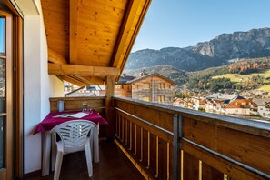 A balcony with a wooden railing, a table with a red tablecloth, and a white chair. - Apartment '5' with Mountain View, Shared Garden and Wi-Fi (Badia)