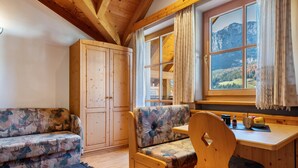 Una habitación acogedora con techo de madera, un sofá, una silla de madera, un escritorio con vistas a las montañas y un armario.