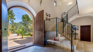A spacious interior with a view through a large arched doorway, a staircase with a metal railing, and a bench near the entrance. - Luxurious villa with sea views and surrounded by nature at 10 min from Andratx (Andratx)