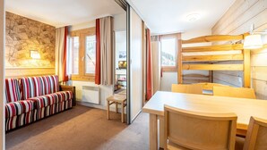 A cozy room with a striped sofa, a wooden dining table, and a bunk bed with a lamp.
