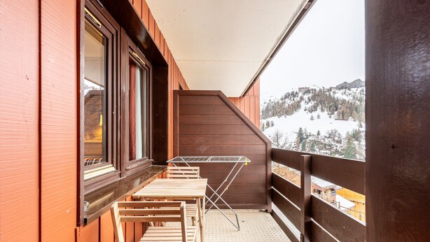 A balcony with a wooden table and chairs, a drying rack, and a view of a snowy mountain.