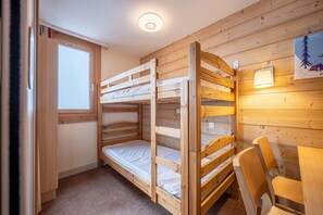Kerrossängyllä varustettu huone, jossa on ikkuna, pöytä tuoleineen ja seinään kiinnitetty valaisin.