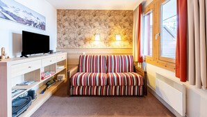 A room with a sofa, a TV, a wall-mounted lamp, and a window with curtains.