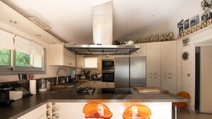 Una cocina moderna con electrodomésticos de acero inoxidable, una isla central con taburetes de bar y un ventanal con cortinas.