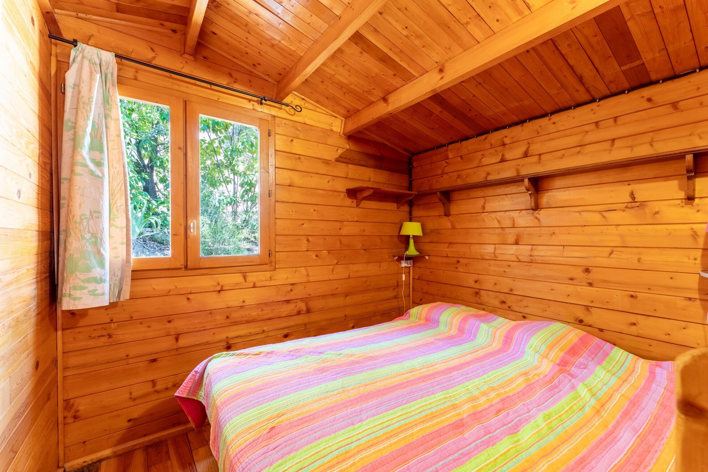 A wooden cabin room with a bed, a window, and a lamp.