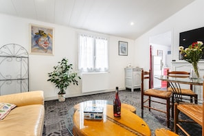 Een woonkamer met een bank, een glazen salontafel, een plant in pot, een fles en een schilderij aan de muur.