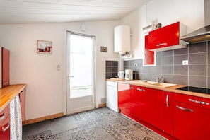 Een keuken met rode kastjes, een witte deur en een betegelde spatwand.