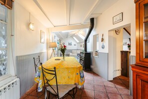 Un comedor con una mesa cubierta con mantel amarillo, sillas, un jarrón con flores y vistas a otra habitación.