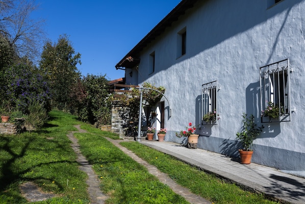 A building with a stone pathway leading to a wooden door, potted plants, and a clear blue sky.