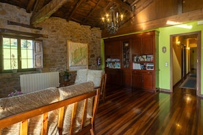 A room with a stone wall, wooden ceiling beams, a wooden bench, a map on the wall, and a wooden cabinet with various items.