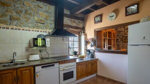 Una cocina con paredes de piedra, armarios de madera, lavavajillas blanco, estufa, microondas y refrigerador.