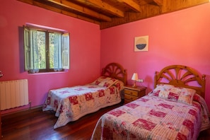 A bedroom with two beds, a window, a radiator, and a wooden ceiling.