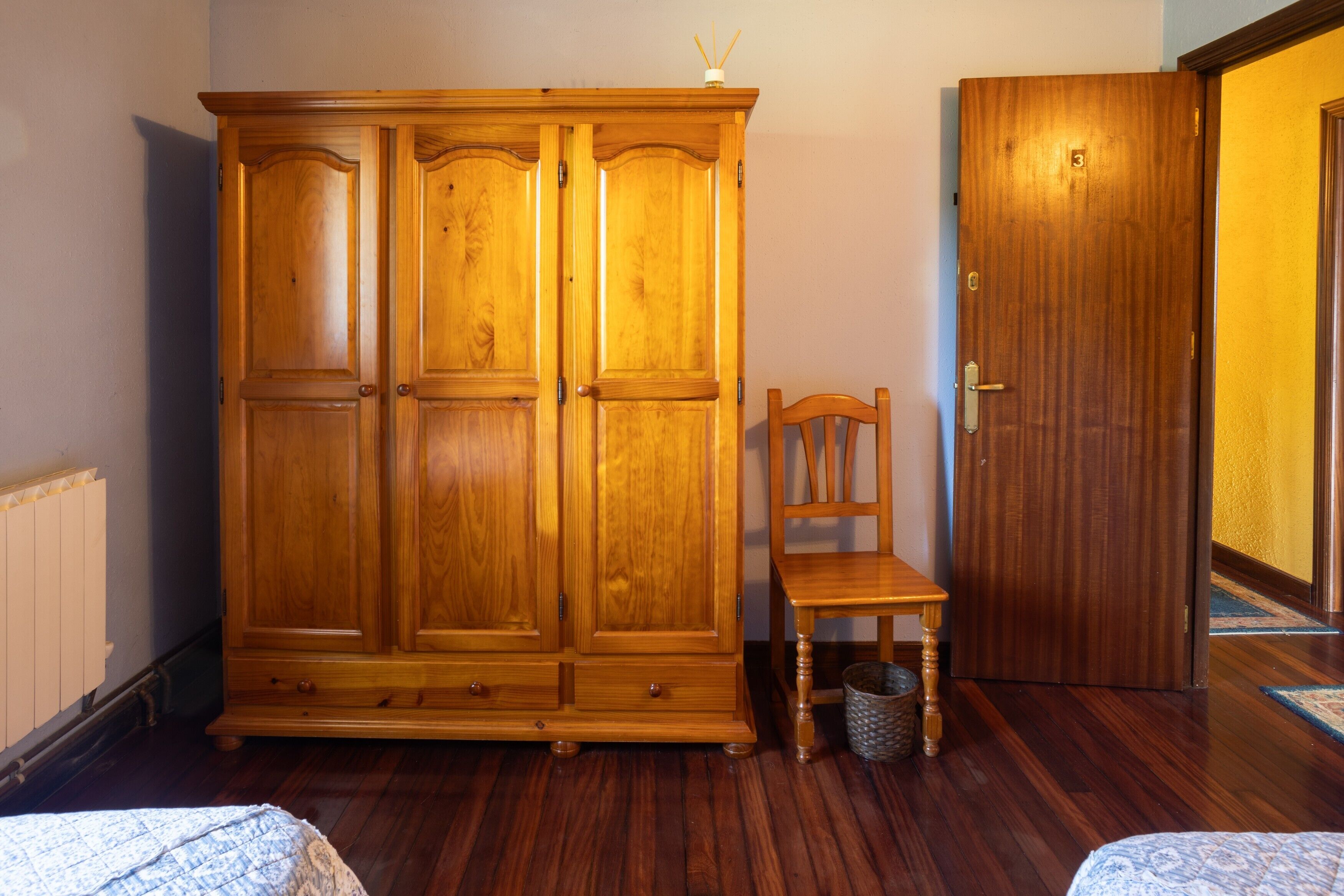 Une pièce avec une armoire en bois, une chaise en bois, une porte et un radiateur.
