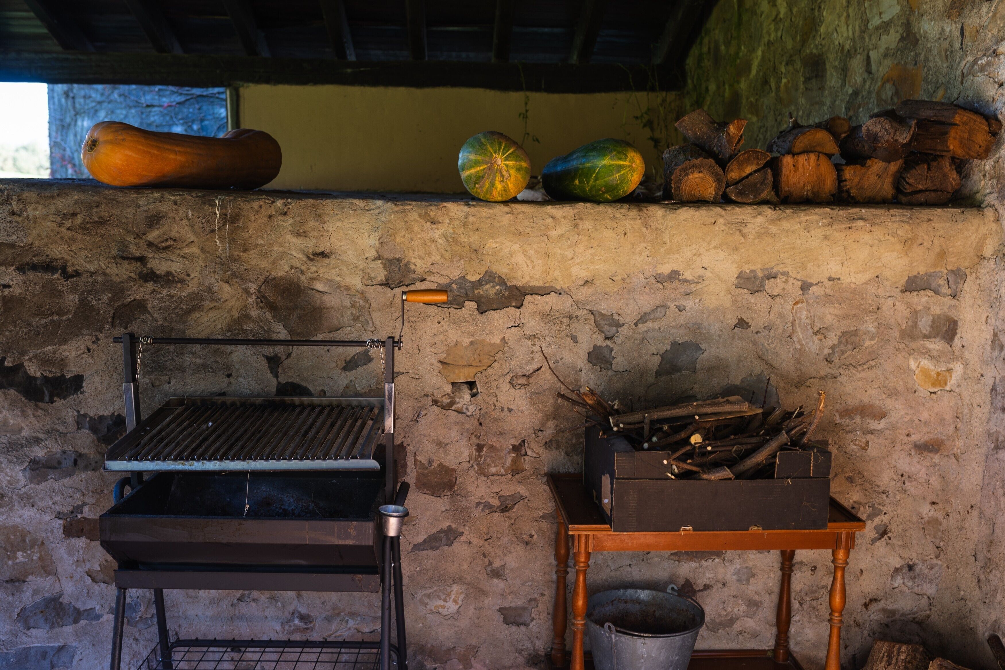 Eine rustikale Küche mit einem Holzkohlegrill, einem Holztisch mit Holzscheiten und einer hängenden Kürbis.