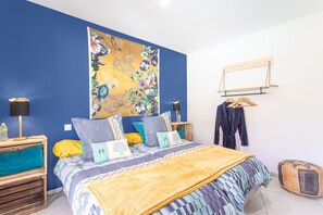 Une chambre à coucher avec un lit, une tapisserie murale, une table de chevet en bois, une robe suspendue et une valise.