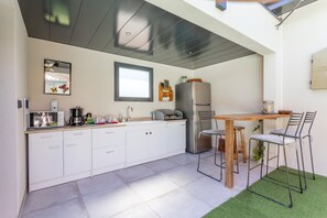 Une cuisine moderne avec des meubles blancs, un réfrigérateur en acier inoxydable, une table en bois et deux chaises en métal.