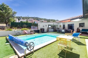 Un jardin avec une piscine, un espace salon couvert et une terrasse aménagée avec du mobilier d’extérieur.