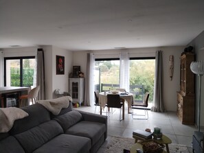 Un salon moderne avec un canapé, une table à manger et une vue sur la verdure environnante.