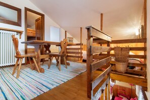 A room with a wooden table and chairs, a striped rug, and a wooden bed with a basket.