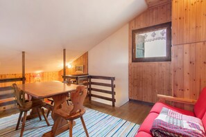 A wooden interior with a dining table, chairs, a red sofa, and a window with lace curtains.
