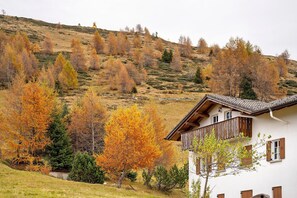 A white building with a balcony, surrounded by autumn trees and a hillside.