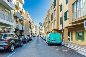 Une rue bordée de voitures garées, des immeubles à plusieurs étages et un ciel dégagé.