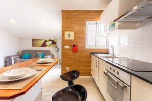 Uma cozinha moderna com uma parede de destaque em madeira, uma área de refeições com mesa e cadeiras de madeira, e um sofá ao fundo.