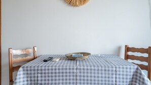 Une nappe à carreaux, un panier en osier, une télécommande et un livre sur une table, avec deux chaises en bois.