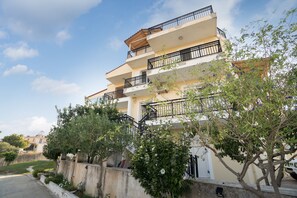 Un edificio residencial de varios pisos con balcones, un jardín y un cielo despejado.