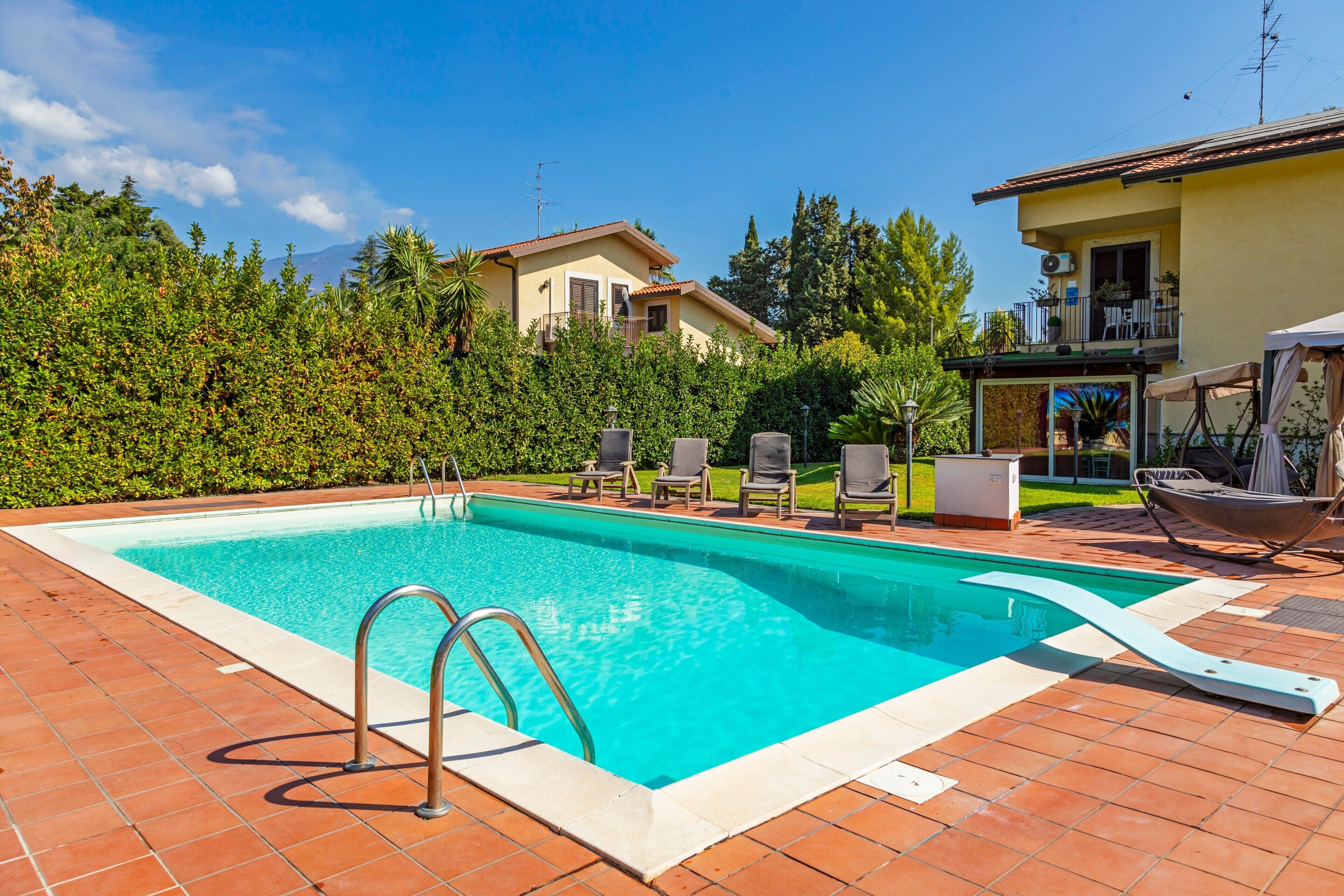 Una piscina rectangular con una escalera metálica, rodeada por un solárium con baldosas.
