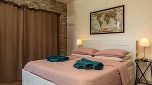 Un lit bien fait, avec une literie rose et des serviettes turquoise, une carte du monde accrochée au mur et deux lampes de chevet.