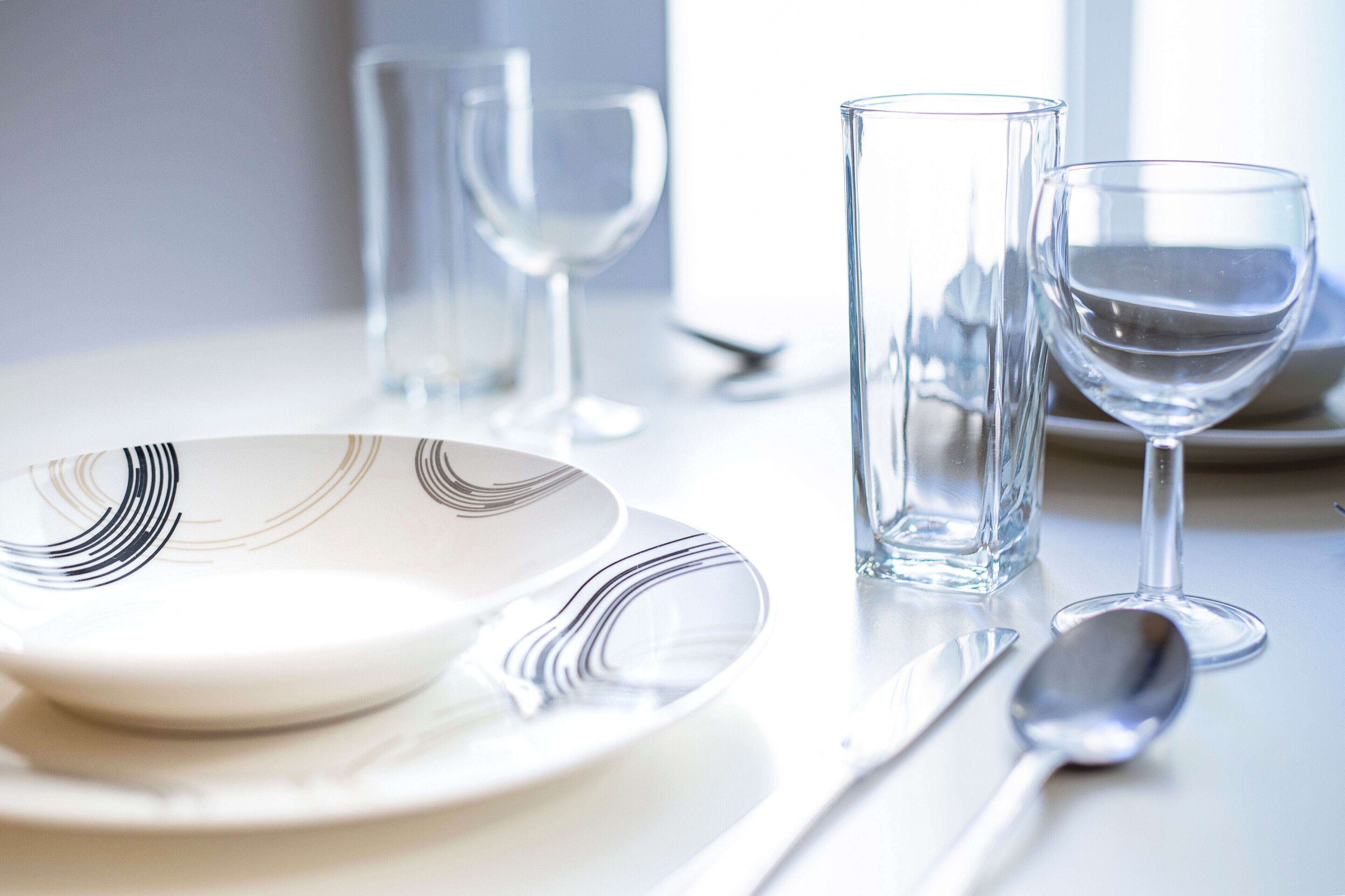 A dining table with a white plate, a spoon, a glass, and a tall glass.