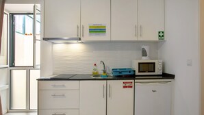 Une petite cuisine équipée avec des meubles blancs, un four à micro-ondes, une bouilloire et un évier.