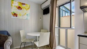 Une pièce comprenant une table à manger, des chaises, un canapé, un appareil de climatisation, un téléviseur et une fenêtre avec des rideaux.