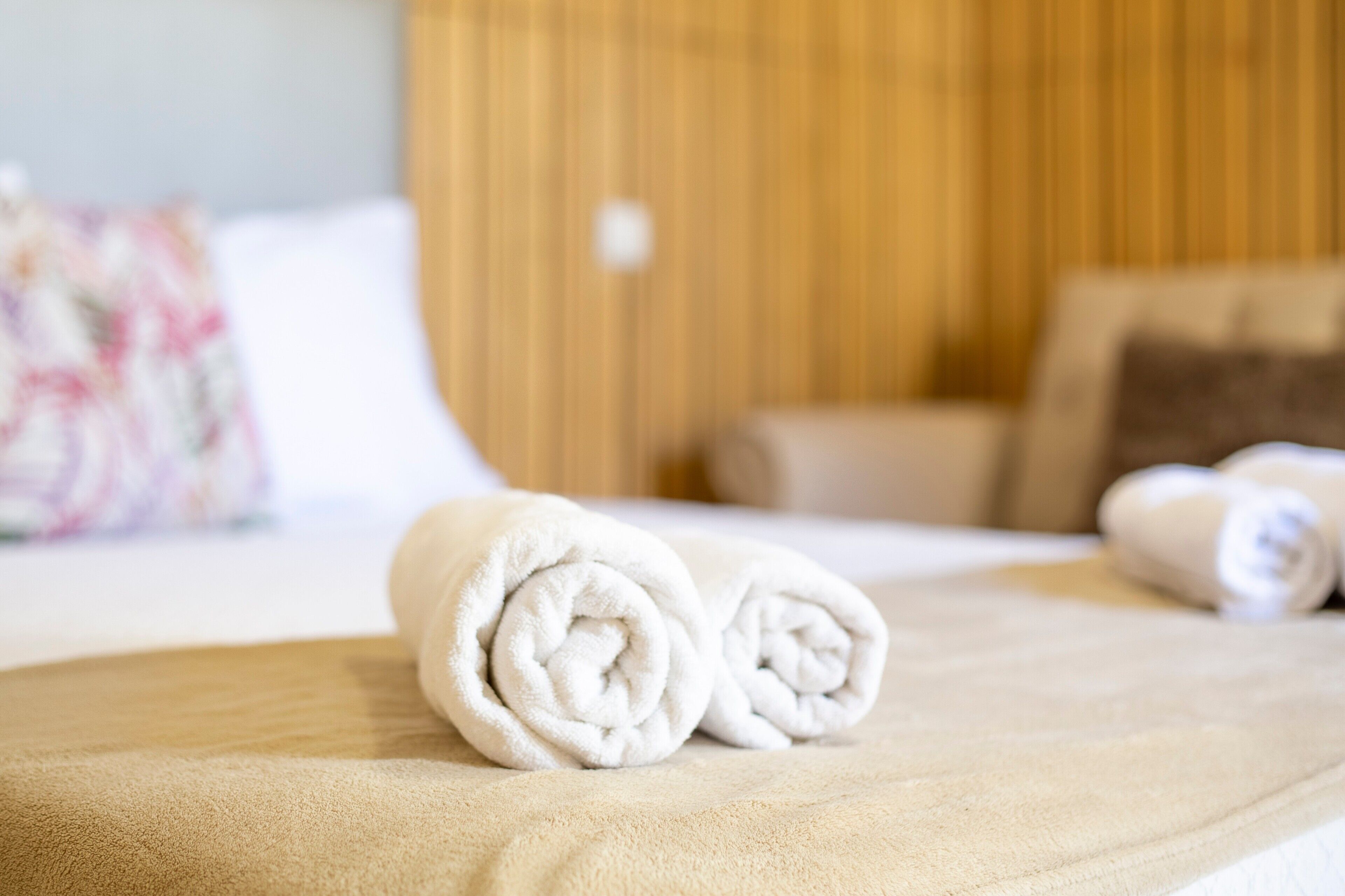 Una cama bien hecha con toallas blancas enrolladas, un cabecero de madera y una almohada estampada con flores.