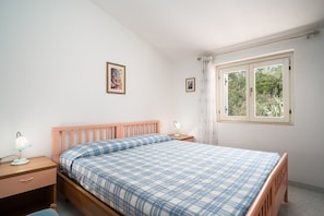 Une chambre à coucher avec un lit en bois, une table de chevet avec une lampe, une fenêtre avec des rideaux et deux tableaux encadrés accrochés au mur.